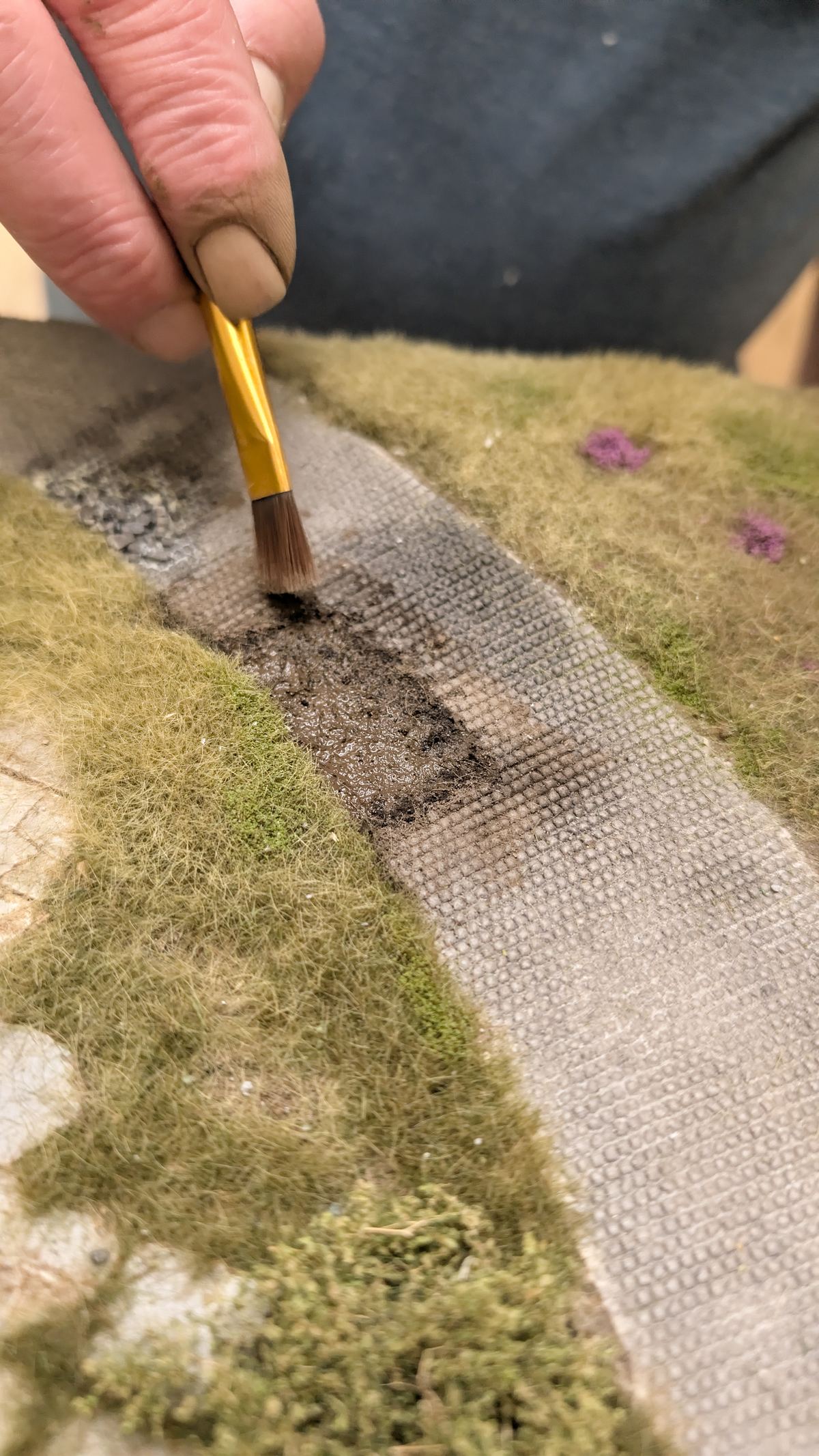Flachpinsel verteilt braunes Pigment entlang der Wegkante